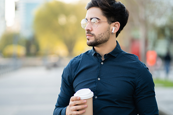 Young man holding a cup of coffee while walking outdoors.